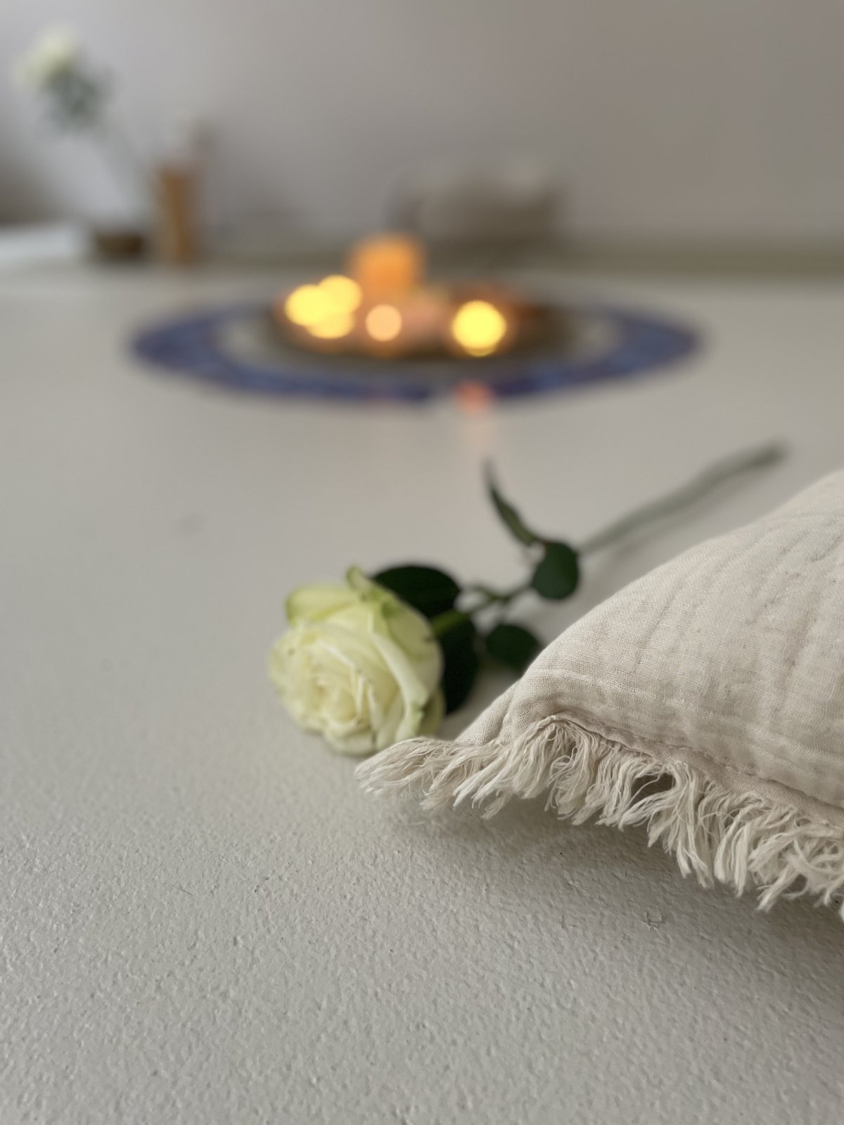 Rose auf einem Leinenkissen, im Hintergrund Kerzenlicht
